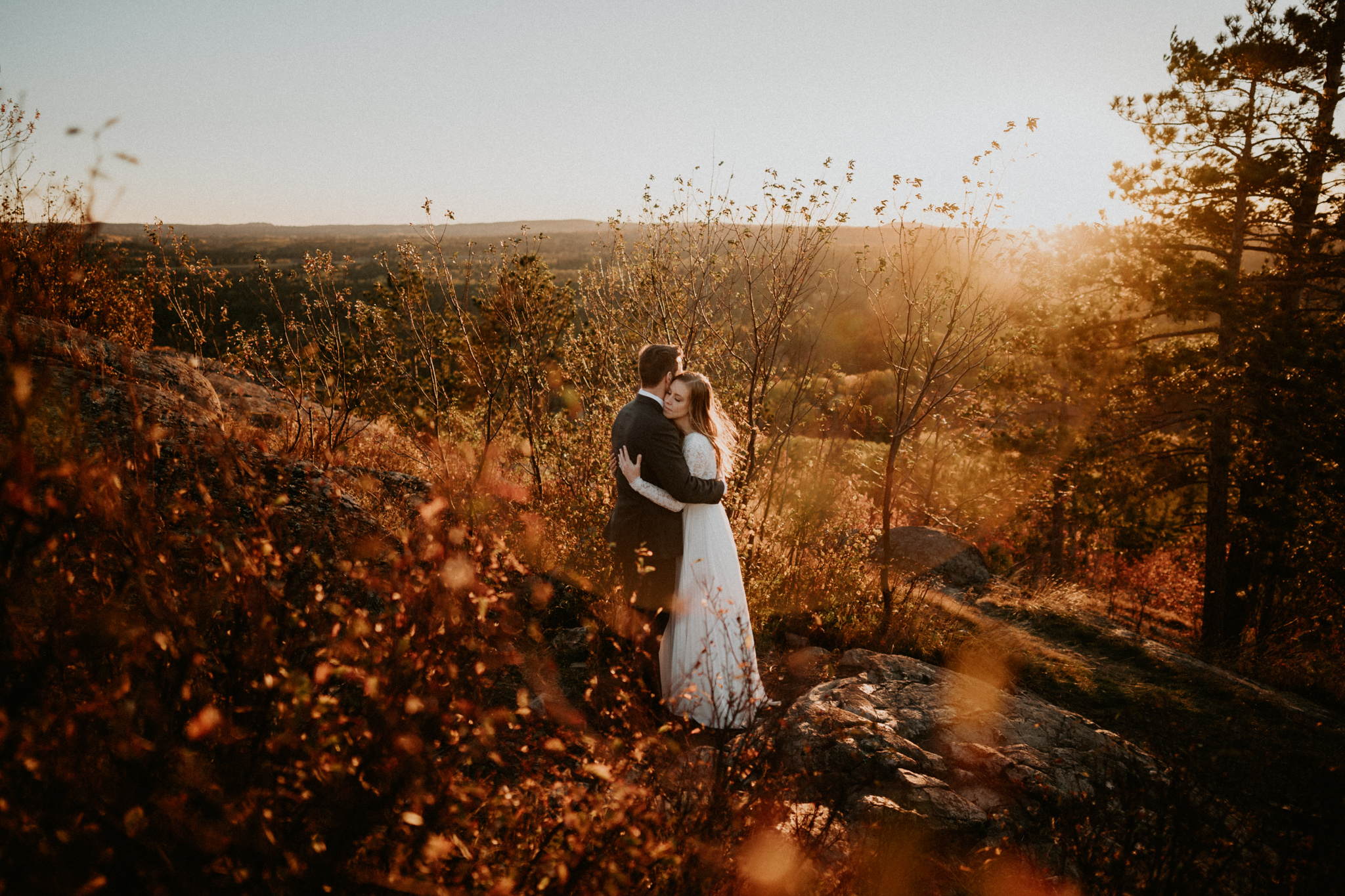 Couple hugging among vibrant fall foliage on overlook near Marquette, Michigan during autumn elopement