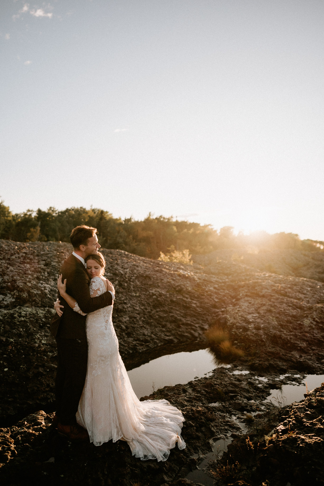 Bride and groom embracing on rocky cliff at sunset in Copper Harbor, Michigan during intimate elopement