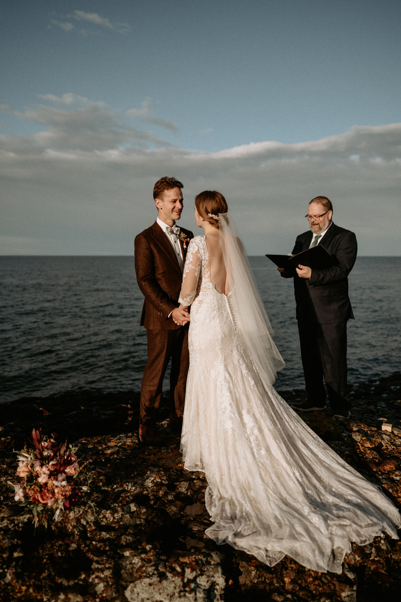 Bride and groom standing on rocky Lake Superior shoreline during an elopement ceremony in Michigan with officiant reading vows